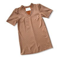 A short-sleeve V-neck top in a warm brownish-beige color, featuring ruffled trim along the neckline and a white brand label inside the collar, displayed on a clean white background.