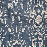 A close-up of a woven fabric pattern featuring a detailed botanical damask design in off-white on a textured slate blue background.