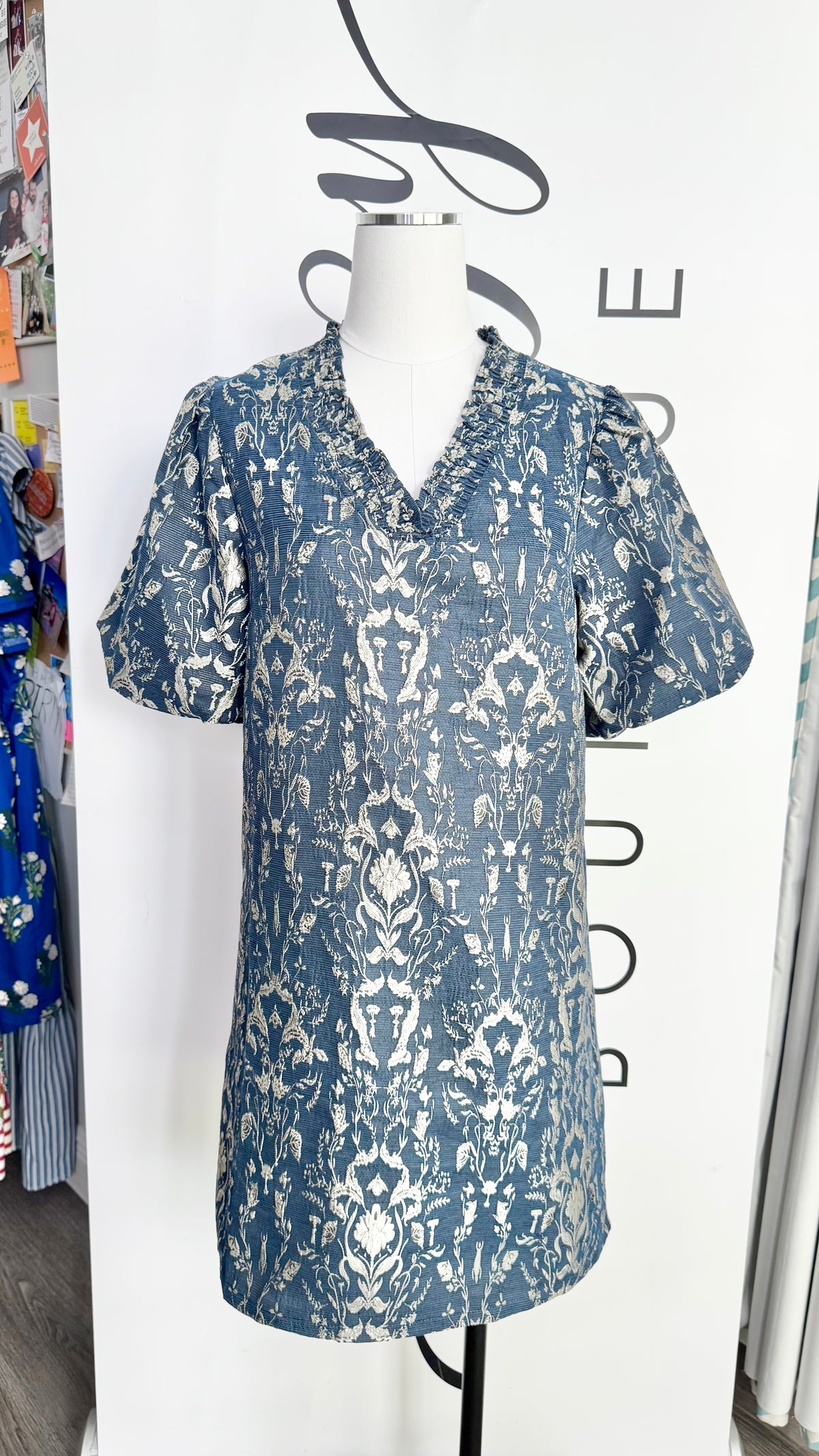 A short-sleeve collared tunic dress with a blue and white damask pattern, displayed on a white mannequin torso in a boutique setting.