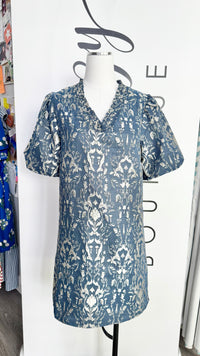 A short-sleeve collared tunic dress with a blue and white damask pattern, displayed on a white mannequin torso in a boutique setting.