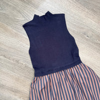 A sleeveless knit mock-neck dress in dark navy blue, paired with a skirt featuring vertical navy and brown stripes, laid flat on a light gray wood-look floor.