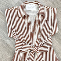 A brown and white vertically striped shirt dress with a tie waist, laid flat on a gray wood-textured surface. The brand name 'L'AGATHA' is visible on the inner neck label.