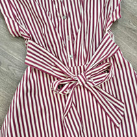 A close-up of a red and white vertically striped shirt dress with a matching fabric tie belt, laid flat on a gray wood-textured surface.
