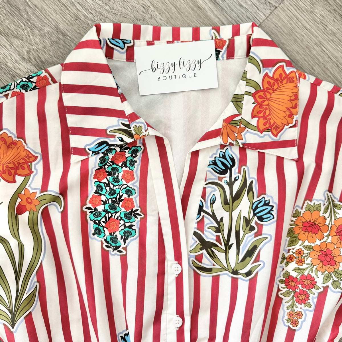 Striped shirt with floral patches and 'Bizzy Lizzy Boutique' tag on a wooden surface