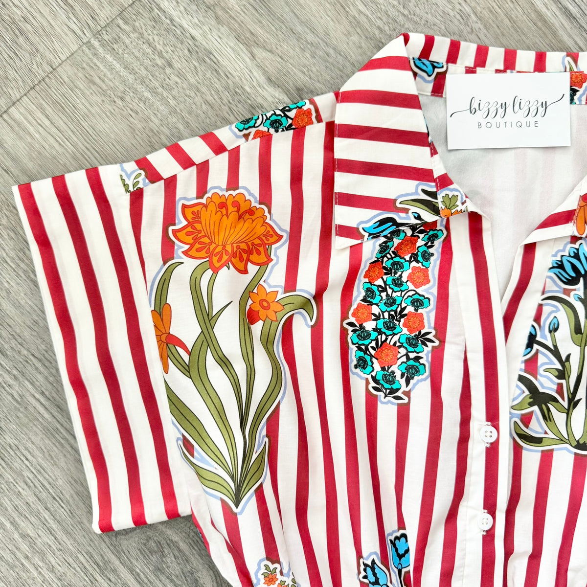 Striped shirt with floral designs on a wooden surface, featuring the brand 'bizzy lizzy'.