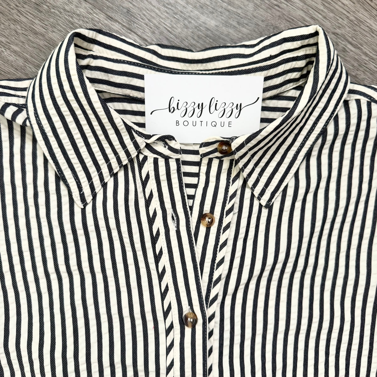 A close-up of a dark blue and cream vertically striped button-down shirt with a pointed collar and a visible neck label reading 'bizzy lizzy BOUTIQUE'.
