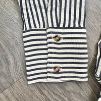 Close-up of a striped fabric garment, likely a shirt or blouse, showing navy and off-white horizontal stripes with two brown buttons on the cuff, laid flat on a gray wood-textured surface.