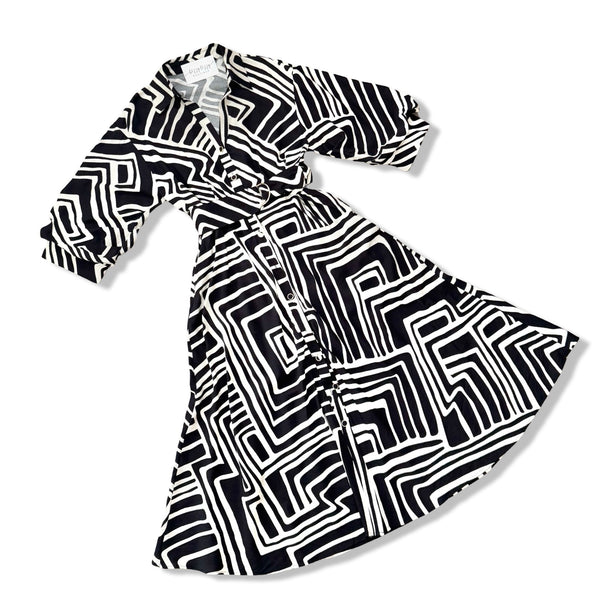 A black and white geometric patterned wrap dress with three-quarter sleeves, displayed on a clean white background.
