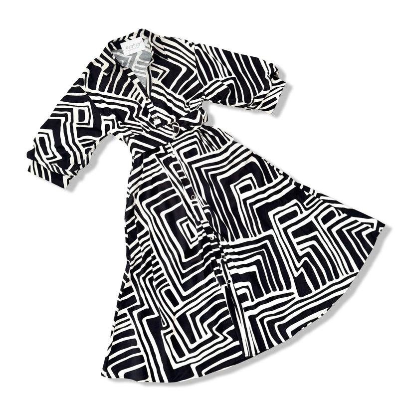 A black and white geometric patterned wrap dress with three-quarter sleeves, displayed on a clean white background.