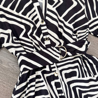 Black and white geometric patterned kimono-style top with a matching belt and gold-tone buttons, laid flat on a gray wood-textured surface.