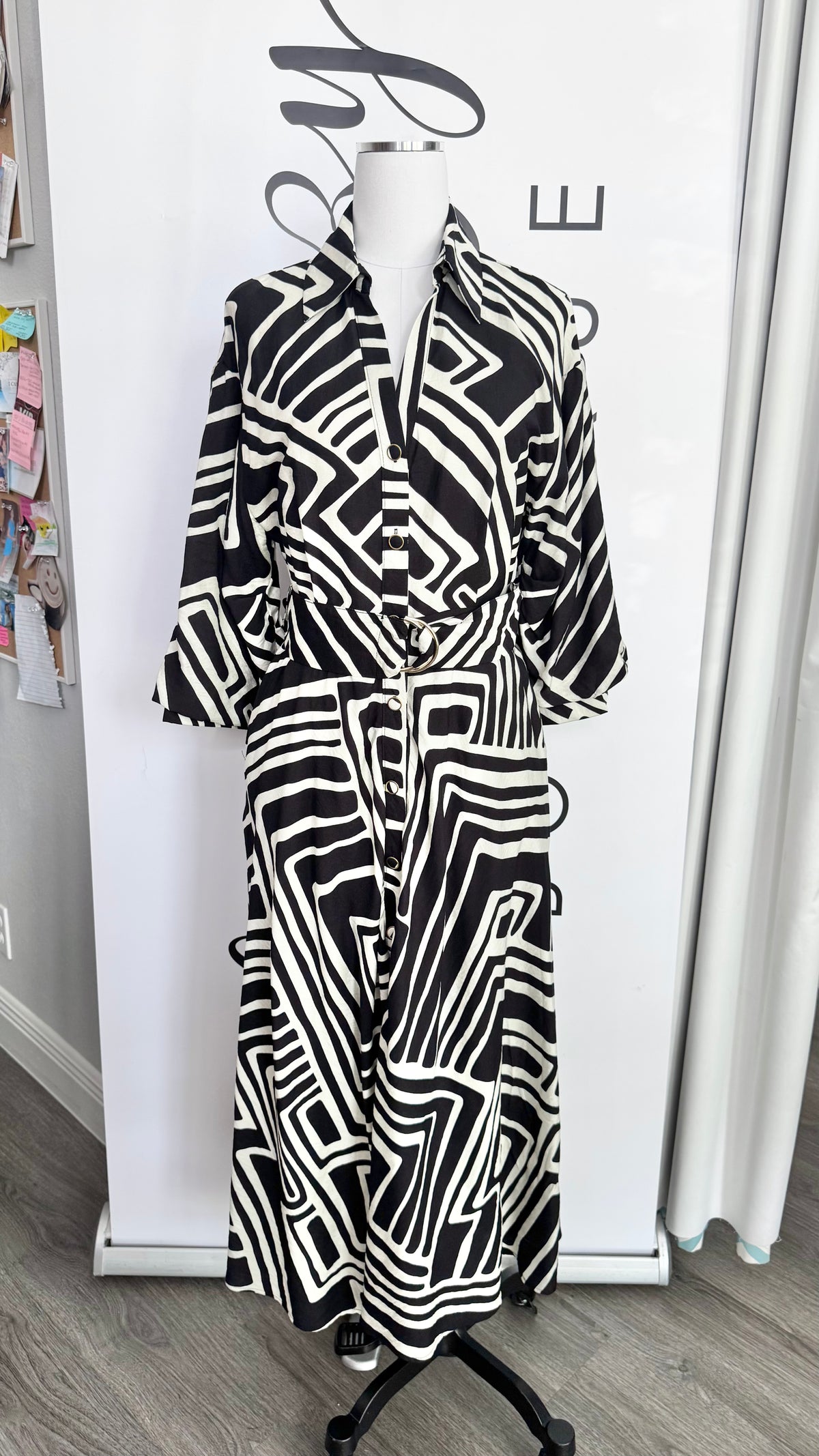 A black and white geometric patterned long-sleeve shirt dress displayed on a mannequin in a boutique setting.