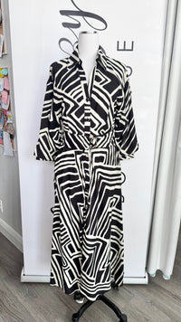 A black and white geometric patterned long-sleeve shirt dress displayed on a mannequin in a boutique setting.