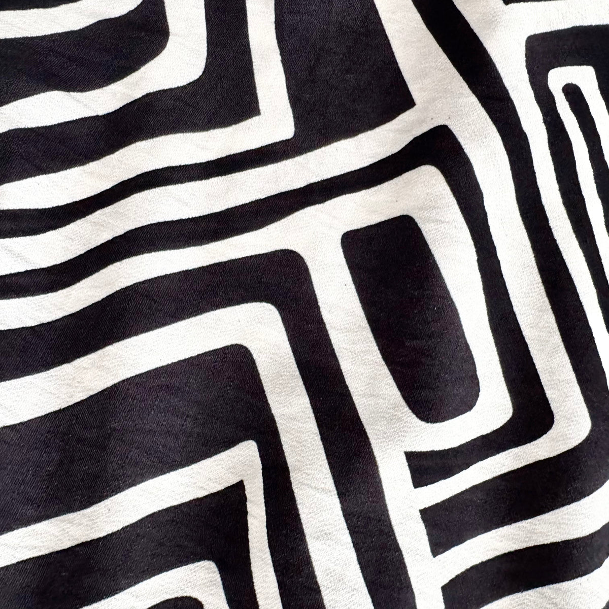 A close-up of a black and off-white fabric with a bold, hand-drawn geometric maze-like pattern.