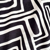 A close-up of a black and off-white fabric with a bold, hand-drawn geometric maze-like pattern.