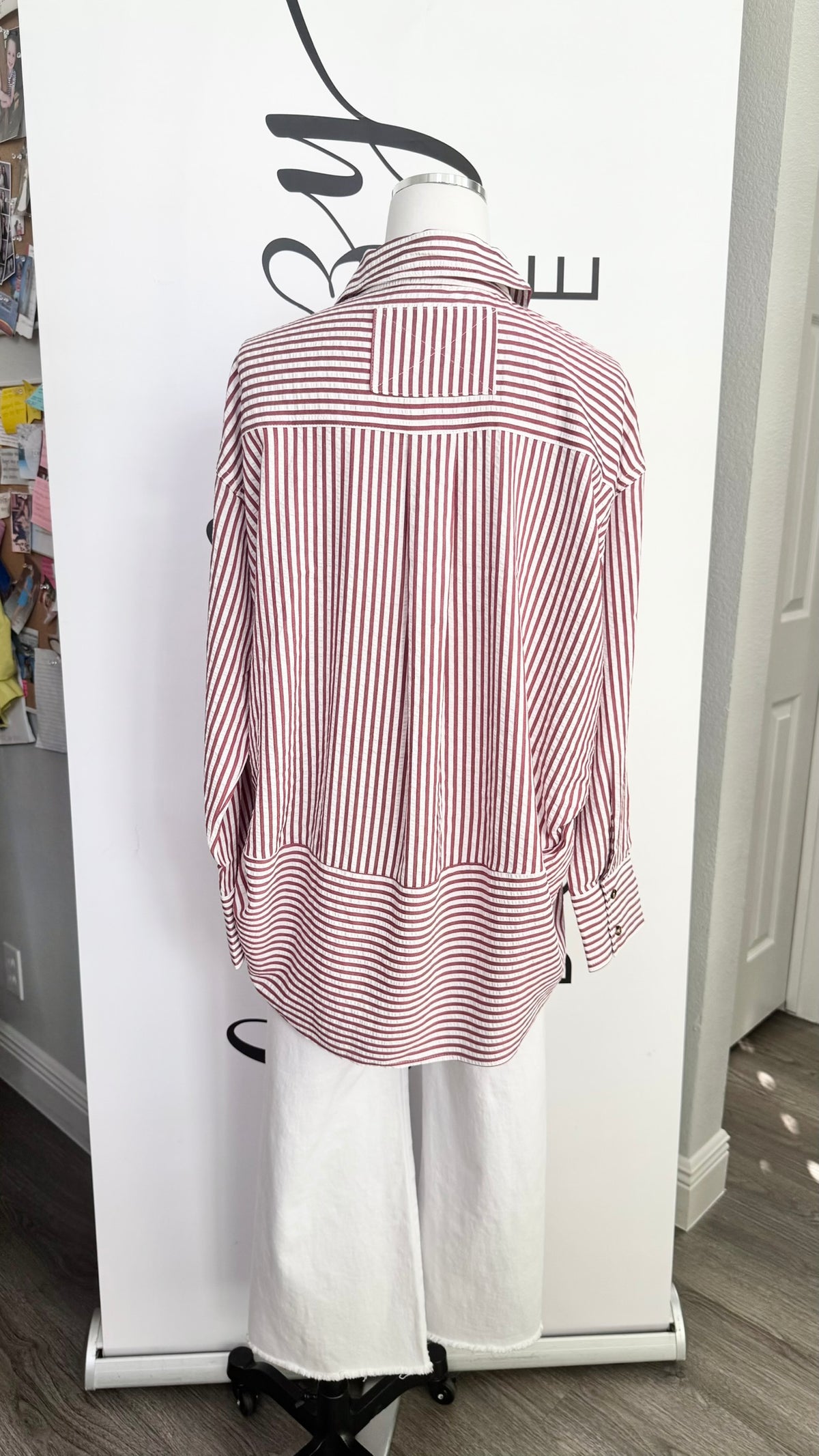 A pink and white vertically striped button-down shirt displayed on a white mannequin torso, paired with white wide-leg pants, set against a white clothing display stand.