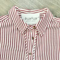 A close-up of a collared button-up shirt with vertical red and white stripes, featuring a white neck label that reads 'bizzy lizzy BOUTIQUE' and brown buttons, laid flat on a light gray wood-textured surface.