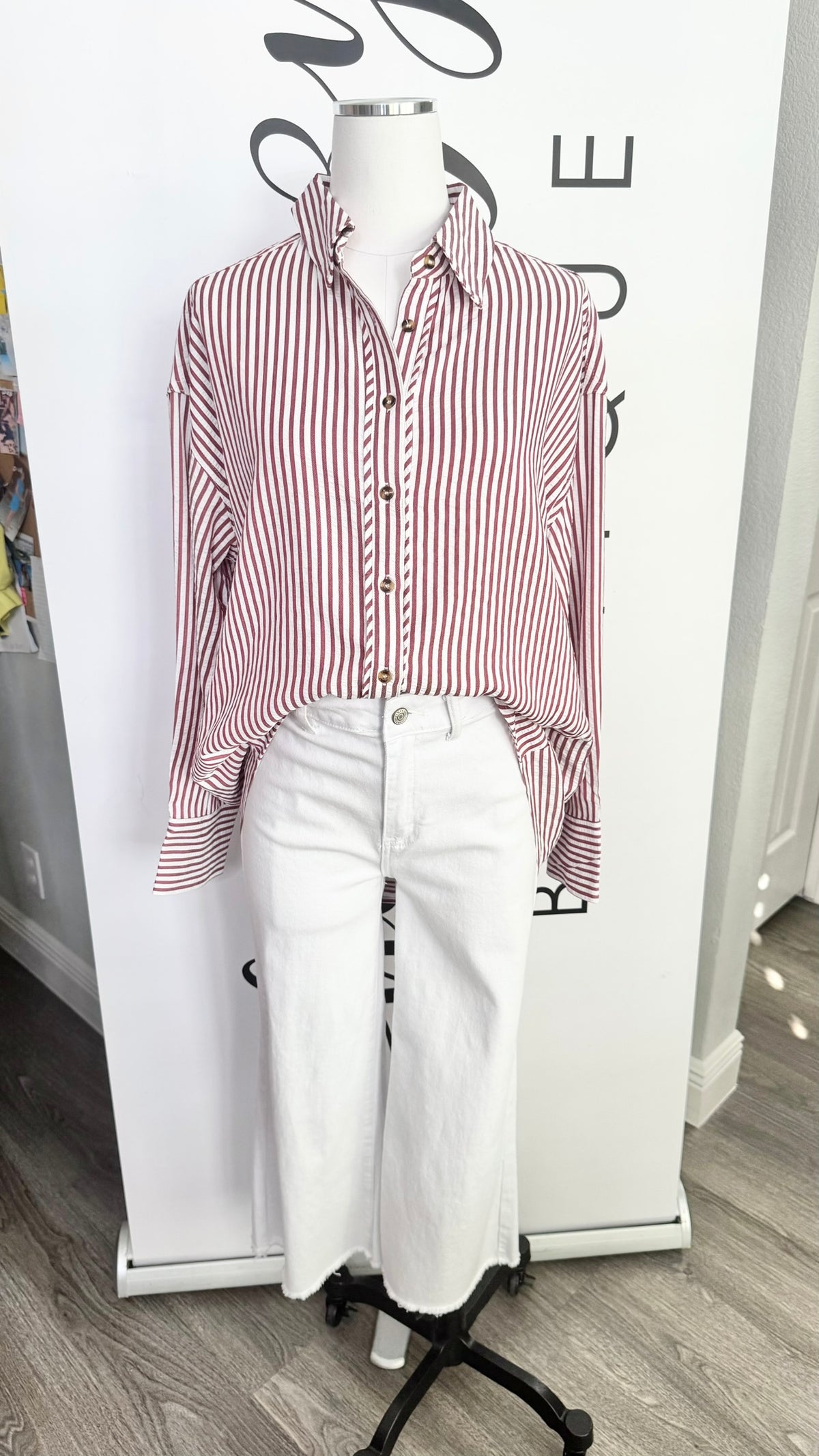 A long-sleeve button-up shirt with vertical red and white stripes, styled on a white mannequin with white cropped pants against a white branded backdrop.