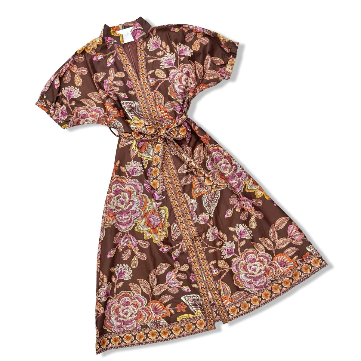 A brown short-sleeve wrap dress with a vibrant floral print in pink, orange, and yellow, featuring a matching waist tie and a patterned border.