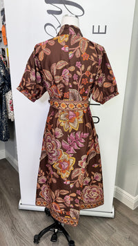 A brown short-sleeve belted dress with a vibrant pink, orange, and yellow floral print, displayed on a mannequin in a boutique setting.