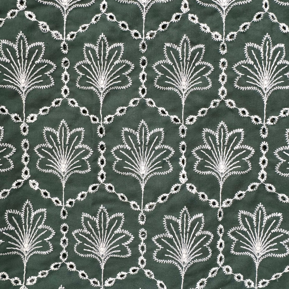 Dark green fabric with a repeating white embroidered or printed floral and geometric trellis pattern.