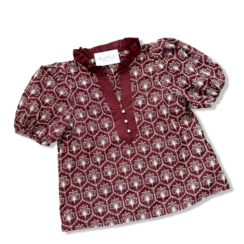 A women's short-sleeve blouse by Mignon, featuring a deep burgundy base with a repeating white floral pattern and a solid burgundy ruffled collar and button placket.