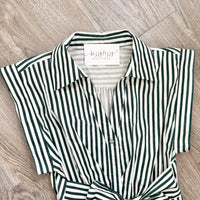 A short-sleeve collared button-front shirt with vertical dark green and off-white stripes, laid flat on a light wood floor. The neck label reads 'bizzy lizzy boutique'.