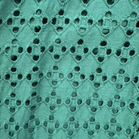 A close-up of a teal green eyelet fabric with a repeating diamond pattern of embroidered borders and circular cutouts.