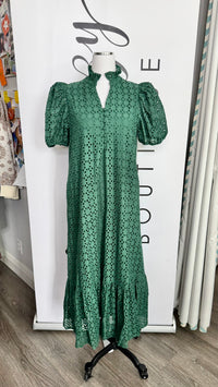 A green eyelet midi dress with puff sleeves and a high mock neck, displayed on a mannequin in front of a boutique backdrop.