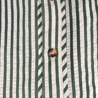Close-up of a striped shirt fabric with vertical green and white stripes, featuring a brown button on the front placket.