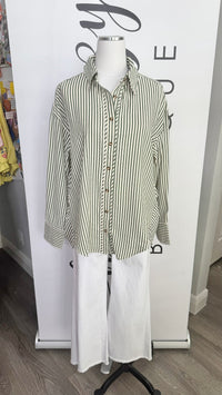 A long-sleeve button-up shirt with vertical green and white stripes, styled on a white mannequin torso with white wide-leg pants in front of a white boutique backdrop.