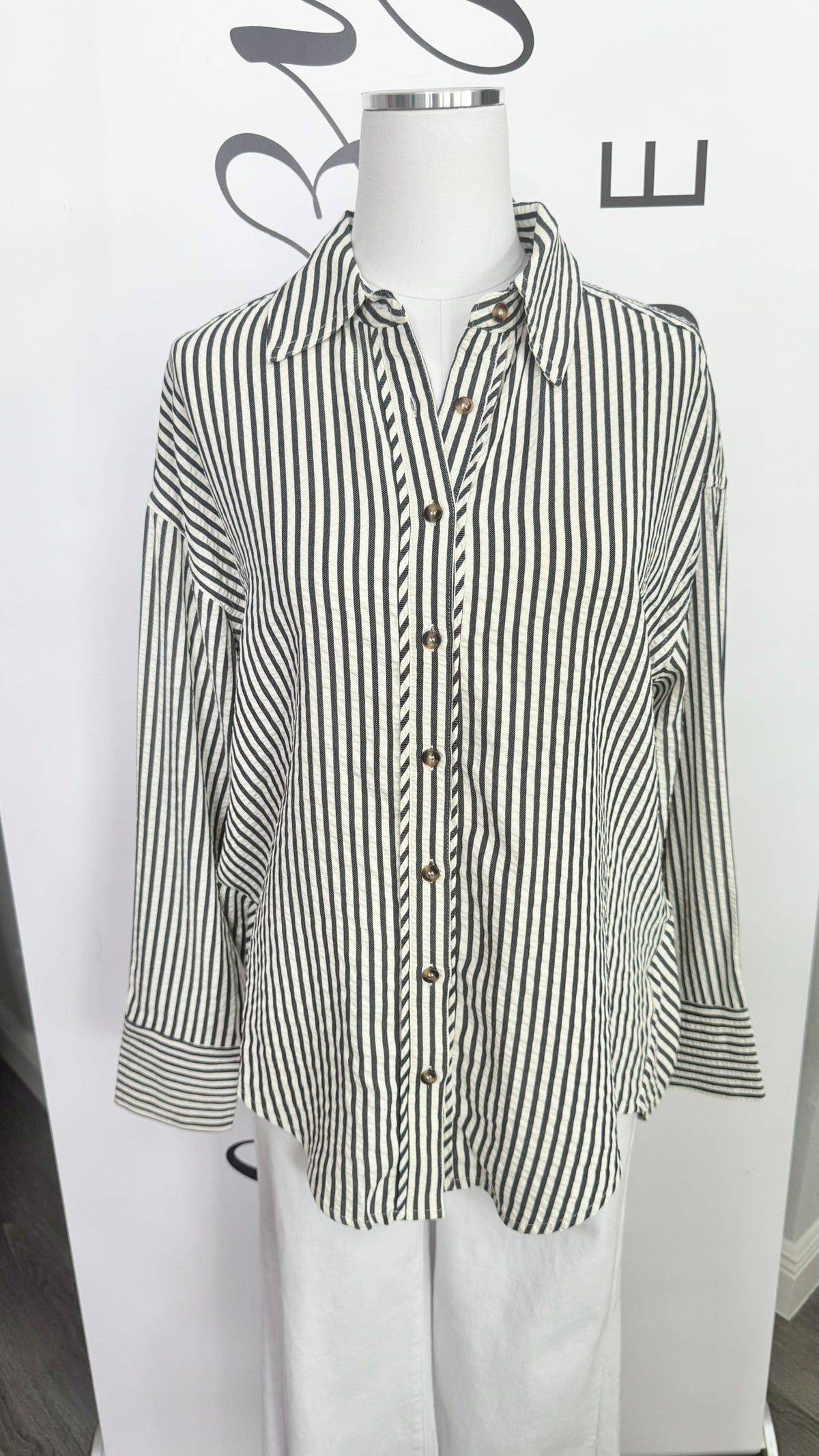 A long-sleeve button-up shirt with vertical black and white stripes, displayed on a white mannequin torso.