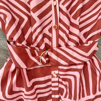 Close-up of a belted button-front garment with a pink and brown wavy geometric pattern and gold-tone buttons and ring detail.
