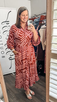 A woman takes a mirror selfie in a boutique showing a rust red and white geometric patterned midi dress with three-quarter sleeves.