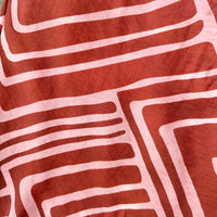 A close-up of a brown and pink fabric with a light pink hand-drawn geometric maze-like pattern.