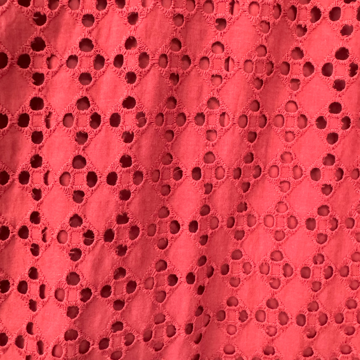 A close-up of a rust orange eyelet fabric with a repeating floral cutwork pattern.