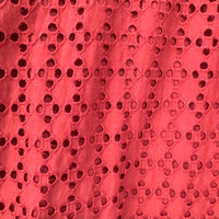 A close-up of a rust orange eyelet fabric with a repeating floral cutwork pattern.