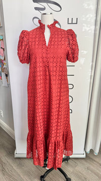 A rust orange eyelet midi dress with puff sleeves and a ruffled hem, displayed on a mannequin in front of a white boutique backdrop.