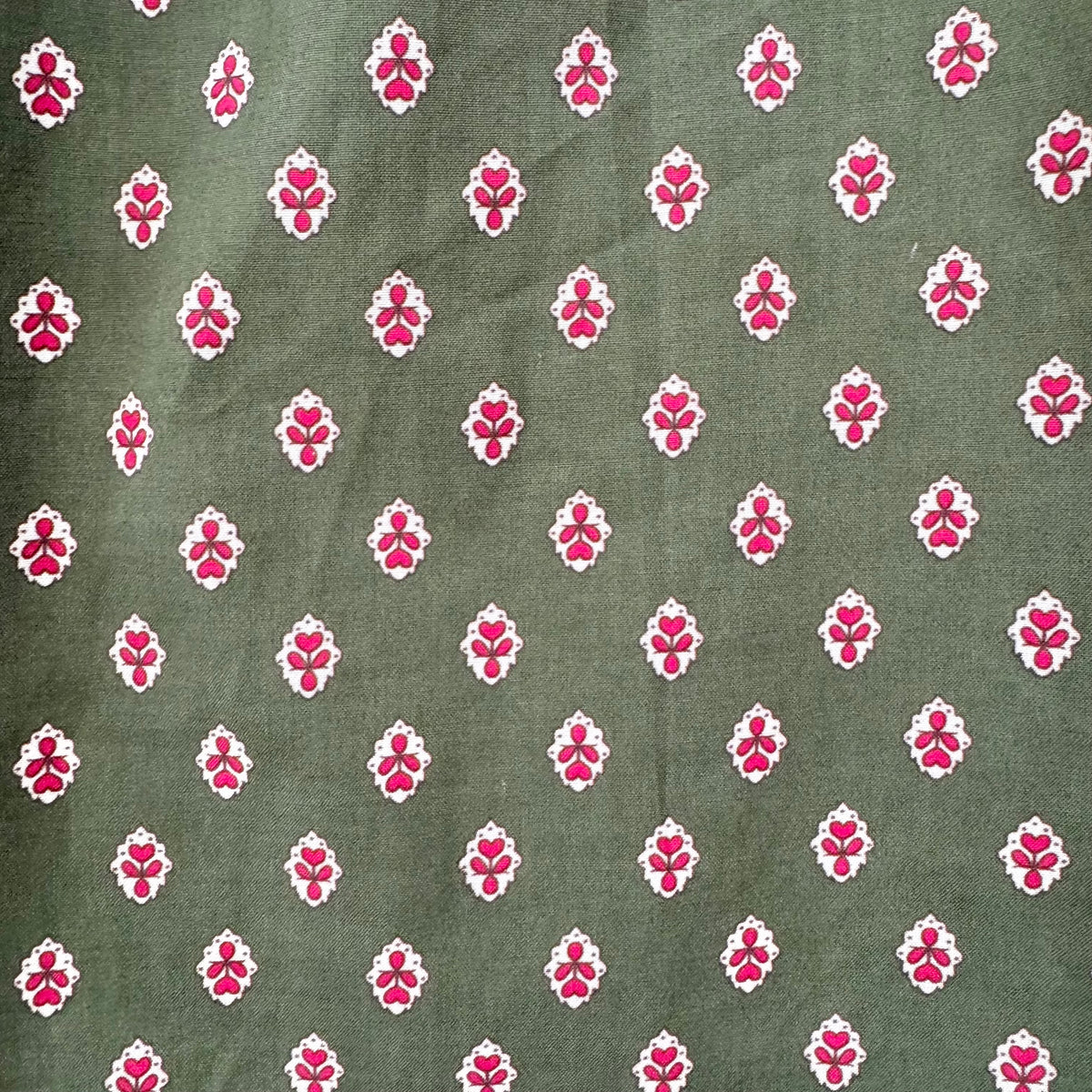 A close-up of a fabric pattern featuring a repeating motif of small pink floral or lotus-like shapes outlined in white, set against an olive green background.