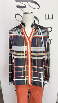 A long-sleeve button-up shirt with a multicolor plaid pattern, displayed on a mannequin torso. The shirt features navy blue, orange, white, and yellow stripes, paired with rust-orange pants.