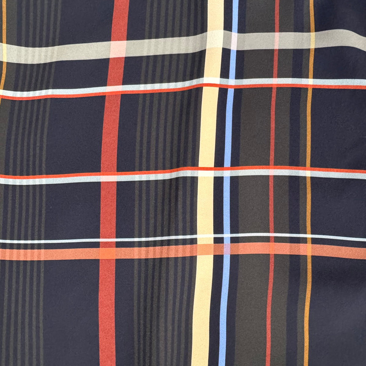 A close-up of a plaid fabric pattern with a dark navy base, featuring intersecting stripes in red, light blue, pale yellow, white, and thin gray lines.
