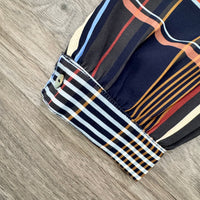 A close-up of a striped shirt sleeve laid flat on a gray wood-grain surface. The fabric features navy blue, cream, orange, red, and light blue stripes, with a buttoned cuff.