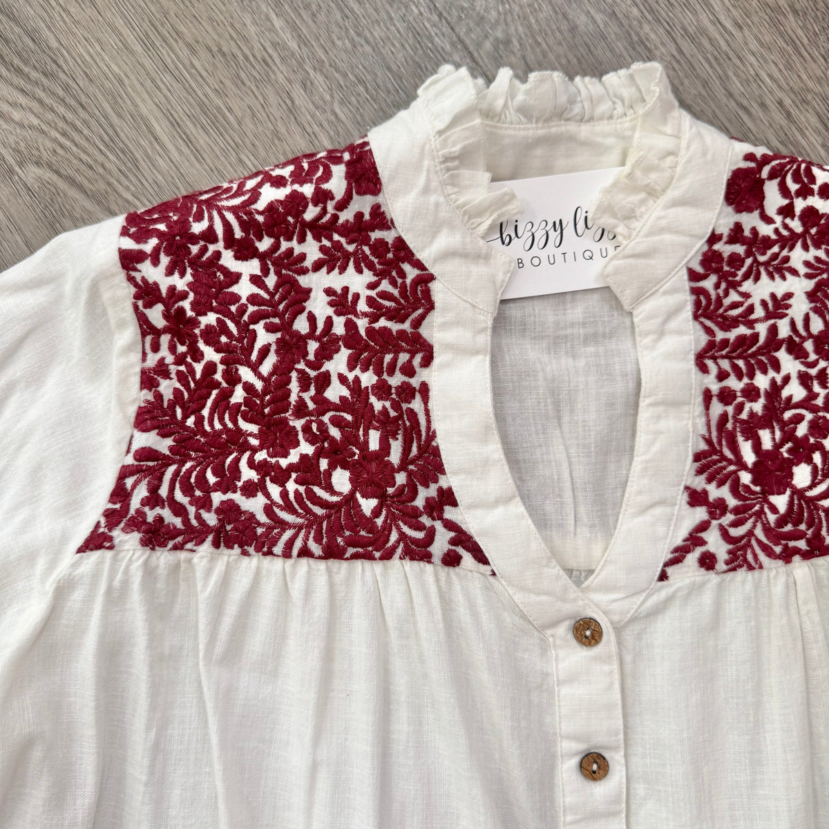White blouse with maroon embroidery on a wooden surface.  Gameday.