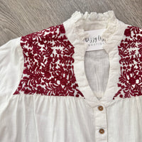 White blouse with maroon embroidery on a wooden surface.  Gameday.