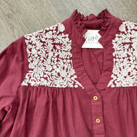 Maroon dress with white embroidered details on a wooden surface