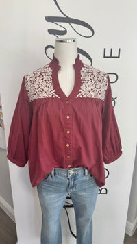 Mannequin wearing a burgundy blouse with embroidered details and blue jeans against a white background.