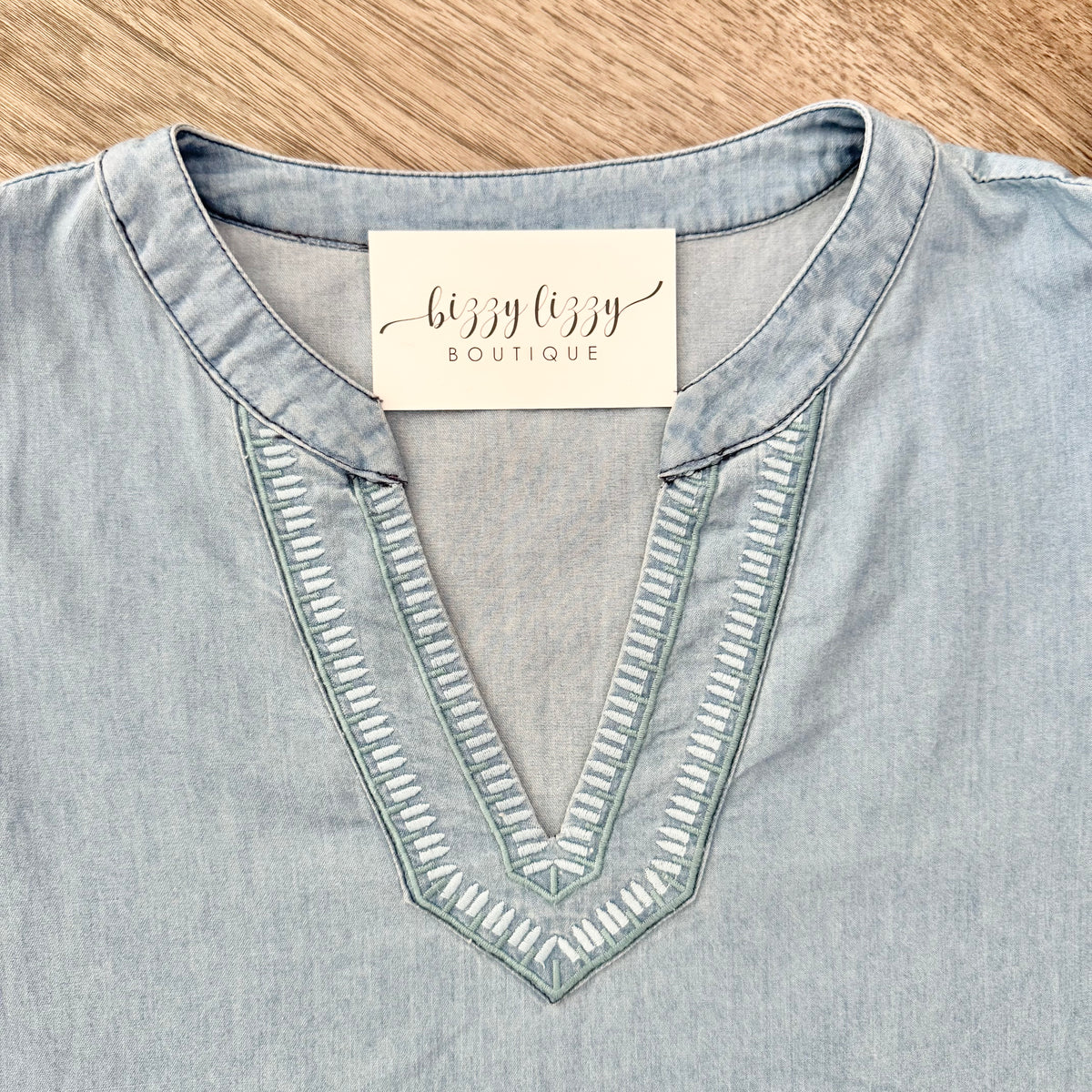 Light blue denim shirt with a 'Lizzy Lizzy Boutique' tag on a wooden surface