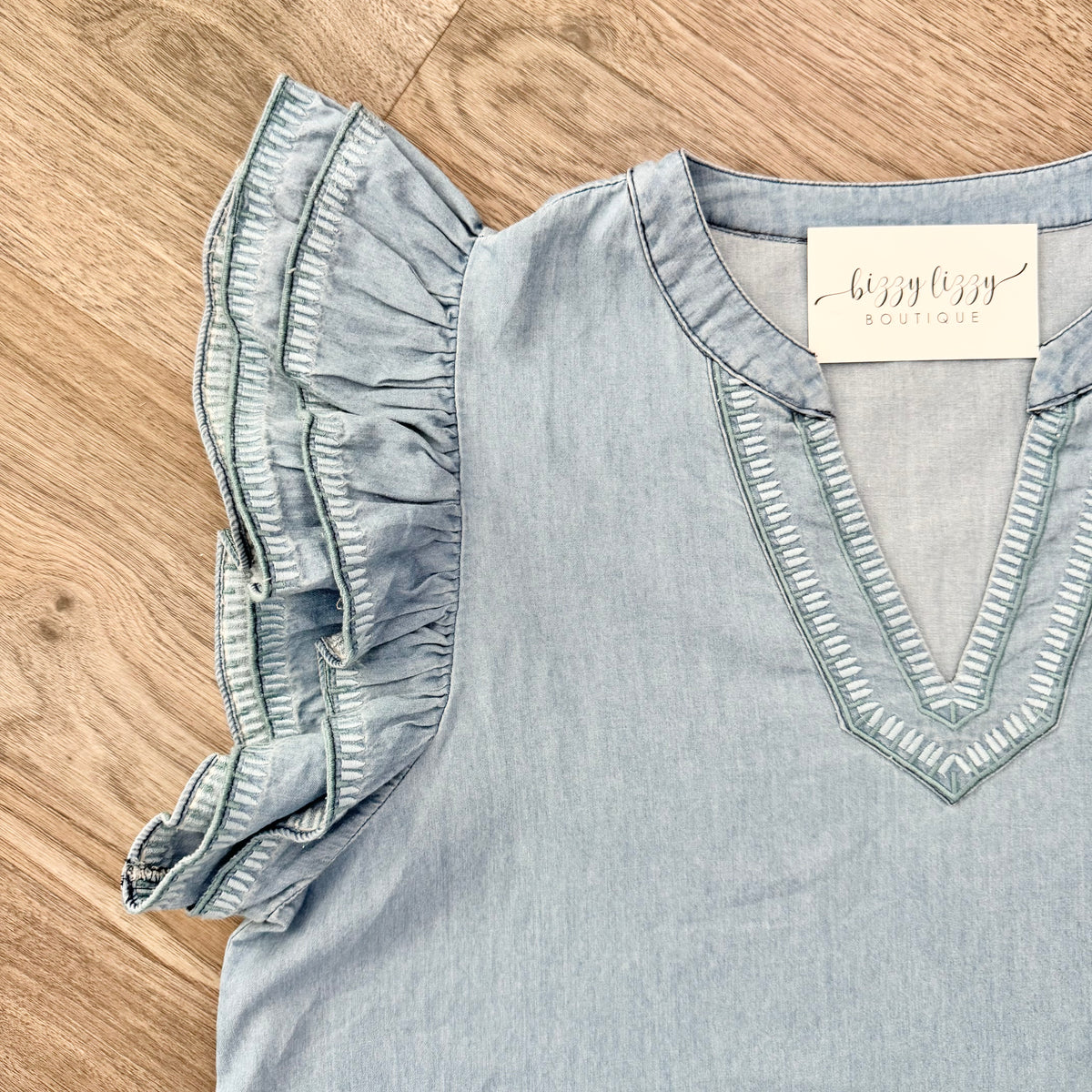 Light blue blouse with ruffled sleeves on a wooden surface, featuring a visible brand tag.