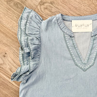Light blue blouse with ruffled sleeves on a wooden surface, featuring a visible brand tag.