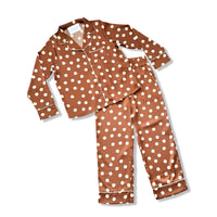 A two-piece pajama set consisting of a long-sleeve button-up top and matching pants, both in a brown satin-like fabric with a white polka dot pattern and white piping details.