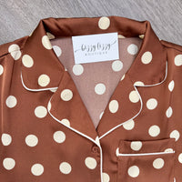A close-up of a brown satin pajama top with cream polka dots and white piping, 